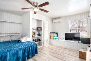 Bedroom featuring a wall mounted AC, a textured ceiling, light hardwood / wood-style flooring, and ceiling fan