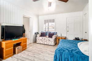 Bedroom with a textured ceiling, ceiling fan, light hardwood / wood-style flooring, and wood walls