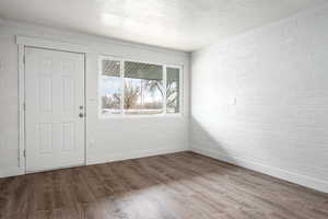 Foyer with wood-type flooring, a textured ceiling, and brick wall