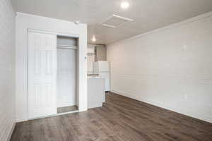 Unfurnished bedroom with brick wall, a textured ceiling, dark hardwood / wood-style floors, white fridge, and a closet