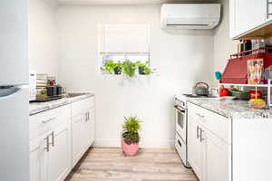 Kitchen featuring light wood-type flooring, white appliances, white cabinets, and an AC wall unit