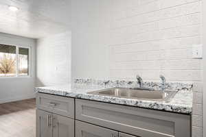 Kitchen with gray cabinetry, sink, a textured ceiling, light hardwood / wood-style floors, and brick wall