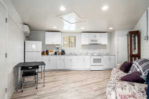 Kitchen featuring white appliances, white cabinets, sink, light hardwood / wood-style flooring, and a wall mounted AC