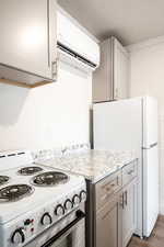 Kitchen with white appliances, dark wood-type flooring, gray cabinets, light stone countertops, and a wall unit AC