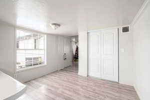 Unfurnished bedroom featuring ornamental molding, light wood-type flooring, a textured ceiling, and a closet