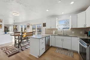 Kitchen with kitchen peninsula, white cabinetry, light hardwood / wood-style flooring, and sink