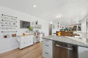 Kitchen featuring dishwasher, light hardwood / wood-style floors, white cabinetry, and hanging light fixtures