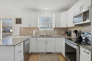 Kitchen with appliances with stainless steel finishes, tasteful backsplash, sink, light hardwood / wood-style flooring, and white cabinetry