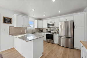 Kitchen featuring kitchen peninsula, white cabinets, light wood-type flooring, and appliances with stainless steel finishes