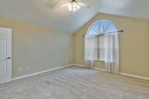 Carpeted spare room with ceiling fan and vaulted ceiling