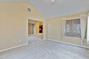 Carpeted empty room featuring high vaulted ceiling