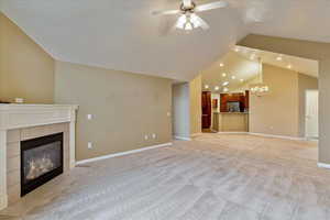 Unfurnished living room with a tile fireplace, ceiling fan with notable chandelier, light colored carpet, and lofted ceiling