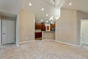 Unfurnished living room with a chandelier, light colored carpet, and high vaulted ceiling