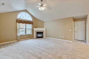 Unfurnished living room with ceiling fan, light colored carpet, a textured ceiling, lofted ceiling, and a tiled fireplace