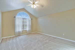 Unfurnished room with a textured ceiling, light colored carpet, ceiling fan, and lofted ceiling