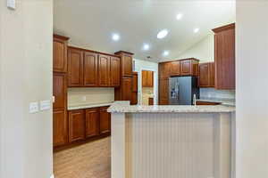 Kitchen with kitchen peninsula, light stone counters, stainless steel fridge with ice dispenser, light hardwood / wood-style floors, and lofted ceiling