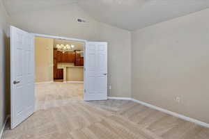 Unfurnished room with light carpet, a textured ceiling, and a notable chandelier