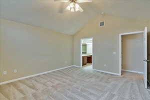 Unfurnished bedroom featuring connected bathroom, ceiling fan, high vaulted ceiling, and light colored carpet