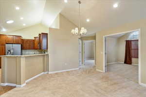 Kitchen featuring light carpet, light stone countertops, stainless steel appliances, vaulted ceiling, and pendant lighting