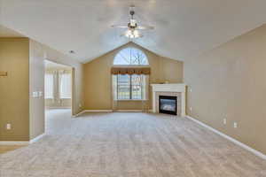 Unfurnished living room with ceiling fan, lofted ceiling, light carpet, and a tile fireplace