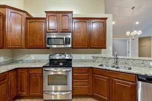 Kitchen featuring light stone countertops, sink, stainless steel appliances, a notable chandelier, and pendant lighting