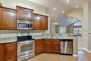 Kitchen with sink, stainless steel appliances, kitchen peninsula, vaulted ceiling, and ceiling fan with notable chandelier