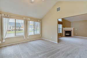 Unfurnished living room with a tile fireplace, plenty of natural light, high vaulted ceiling, and light colored carpet