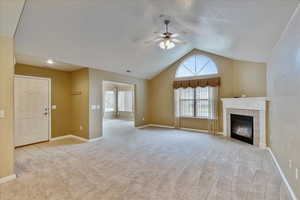 Unfurnished living room featuring ceiling fan, plenty of natural light, light colored carpet, and lofted ceiling