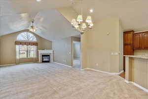 Unfurnished living room featuring a tile fireplace, ceiling fan with notable chandelier, light colored carpet, and vaulted ceiling