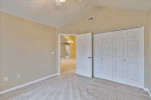 Unfurnished bedroom featuring ceiling fan with notable chandelier, lofted ceiling, light carpet, and a closet