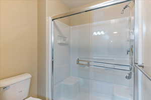 Bathroom featuring a shower with door and toilet