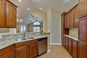 Kitchen featuring stainless steel dishwasher, light stone counters, sink, and vaulted ceiling