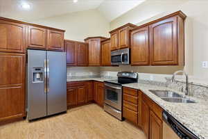 Kitchen featuring sink, vaulted ceiling, appliances with stainless steel finishes, light hardwood / wood-style floors, and light stone counters