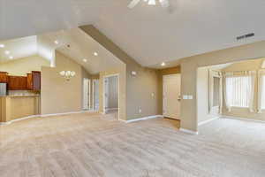 Unfurnished living room featuring ceiling fan with notable chandelier, light colored carpet, and lofted ceiling