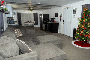 Living room featuring carpet floors, ceiling fan, crown molding, and beamed ceiling