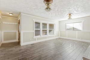 Unfurnished dining area with hardwood / wood-style floors, a textured ceiling, and ornamental molding