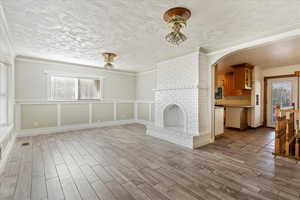 Unfurnished living room with a fireplace, light hardwood / wood-style floors, a textured ceiling, and ornamental molding