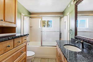 Full bathroom with tile patterned floors, a textured ceiling, combined bath / shower with glass door, toilet, and vanity