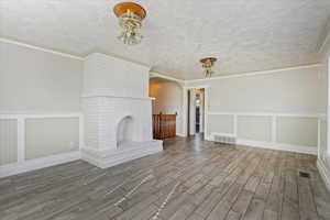 Unfurnished living room featuring a fireplace, wood-type flooring, a textured ceiling, and ornamental molding