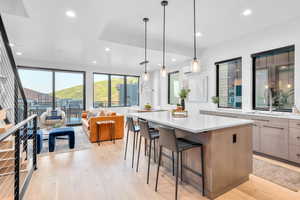 Kitchen with sink, hanging light fixtures, light hardwood / wood-style flooring, a spacious island, and a kitchen bar