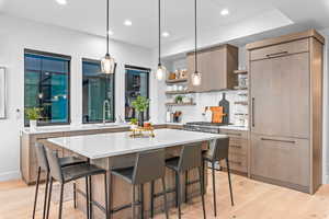 Kitchen with a center island, sink, hanging light fixtures, high end stainless steel range, and light hardwood / wood-style flooring