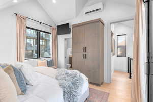 Bedroom with connected bathroom, light wood-type flooring, a wall unit AC, and vaulted ceiling