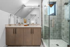 Bathroom with vanity, a shower with door, and lofted ceiling