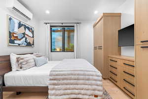 Bedroom with light wood-type flooring and a wall mounted AC