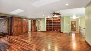 Unfurnished living room with dark hardwood / wood-style floors, ceiling fan, ornamental molding, and a skylight