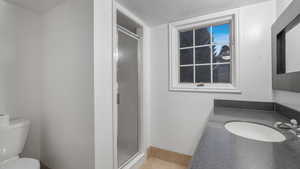 Bathroom featuring walk in shower, tile patterned floors, a textured ceiling, toilet, and vanity