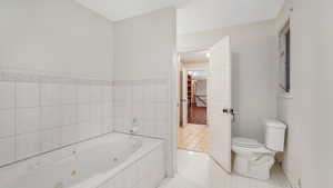 Bathroom with tile patterned floors, a relaxing tiled tub, and toilet