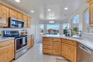 Kitchen featuring appliances with stainless steel finishes, light brown cabinetry, sink, a chandelier, and light tile patterned flooring