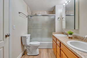 Full bathroom with vanity, a textured ceiling, shower / bath combination with glass door, hardwood / wood-style floors, and toilet