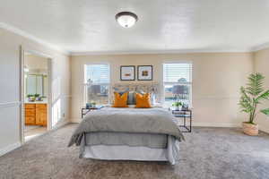 Primary Bedroom featuring ensuite bathroom, new carpet, ornamental molding, and multiple windows